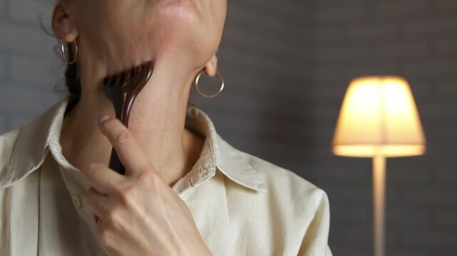 Woman performing neck massage with gua sha tool. Young woman practicing a rejuvenating facial and neck self-massage using a gua sha scraping tool for lymphatic drainage, skin tightening
