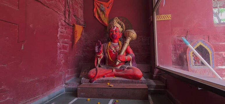 Ancient Orange Hindu Deity Statue in Sitting Position with Mace Weapon Inside an Old Temple Shrine