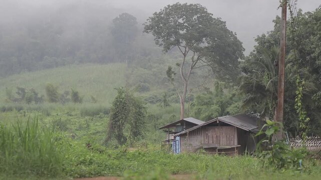 A rustic wooden house nestled in lush green mountains with heavy morning mist in Prachuap Khiri Khan, Thailand. Peaceful rural countryside scene