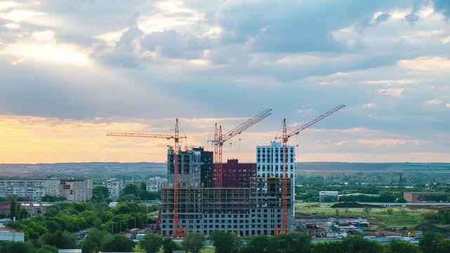 time-lapse, clouds quickly fly over the houses under construction at sunset, and the sun sets behind the horizon