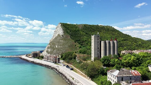 Aerial view of Chirakman Cape featuring white cliffs, industrial silos, and a coastal road along the turquoise sea in Kavarna, Dobrich Province, Bulgaria.