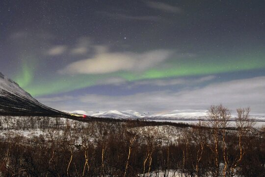 Northern lights (aurora borealis) over deep snow-covered mountains and birch trees, round cabin, Abisko National Park, Lapland, Norrbottens l&auml;n, Sweden