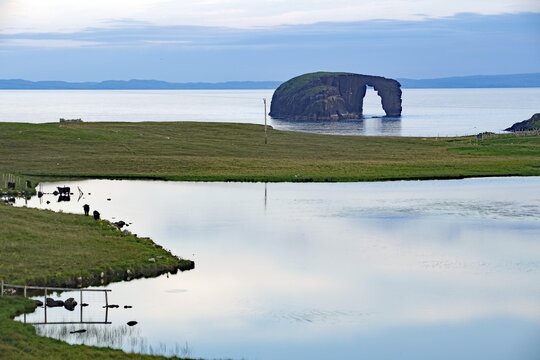 Calm lake with grassy shores and a rock formation on the horizon, dore holm Dore Holm, Hillswick, Eshaness, Shetland Islands, Scotland, United Kingdom