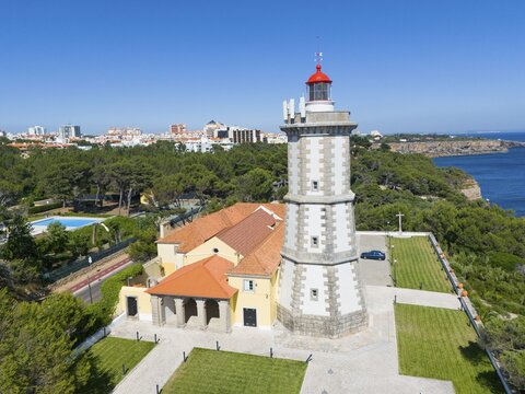 A lighthouse with a red top next to a building with a view of the forest and the sea, aerial view, Farol da Guia, Cabo da Guia, Cascais, Lisbon, Lisboa, Portugal