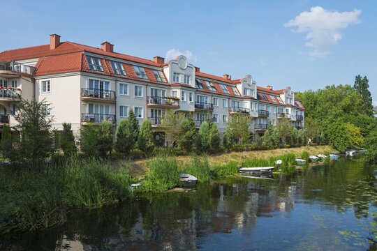 Modern residential buildings on a quiet riverbank with small boats and lush greenery in a summery ambience, Ełk, Elk, Lyck, Elk River, Warmia-Masuria, Poland