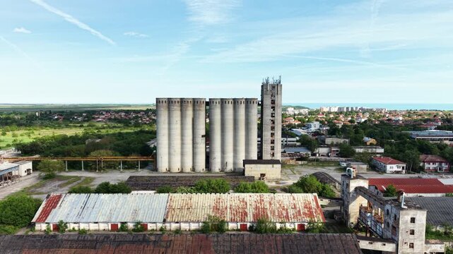 Aerial view of large concrete grain silos and industrial warehouses with rusted roofs in the coastal town of Balchik, Dobrich Province, Bulgaria.