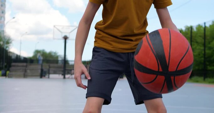 Young boy plays basketball on outdoor court. He dribbles ball skillfully while enjoying sunny day. Excitement fills atmosphere during basketball practice