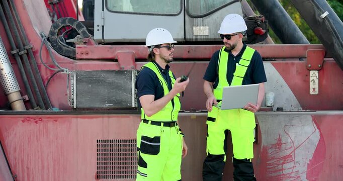 Adult Caucasian male logistics crew use laptop beside reach stacker, reviewing freight data, cargo record, container inspection, safety compliance, yard planning, shipment tracking during outdoor work