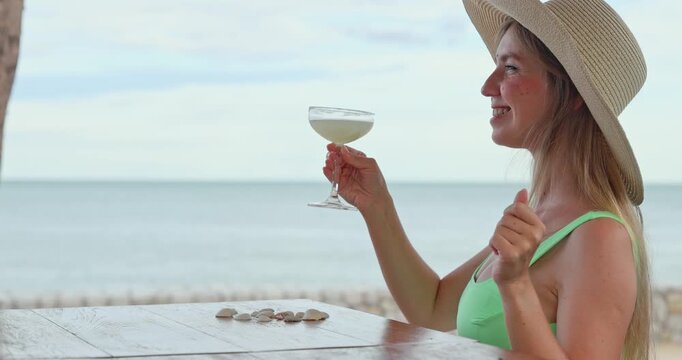 Woman dancing with cocktail glass, sitting at wooden table by seaside, tropical beach resort background, summer vacation travel and leisure lifestyle