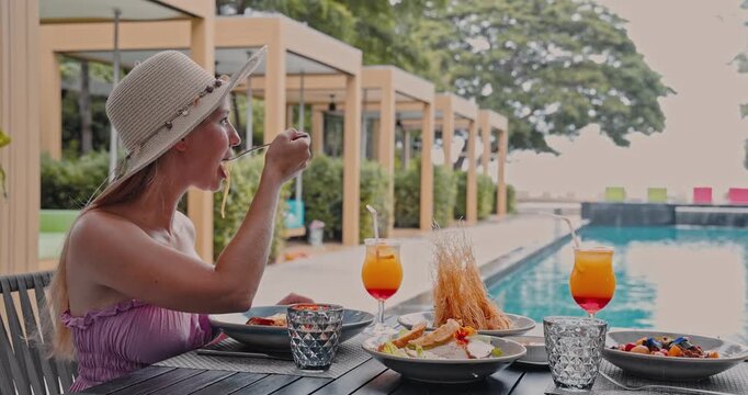 Woman wearing straw hat eating pasta lunch, luxury outdoor poolside dining area, summer vacation lifestyle, high-end travel resort marketing