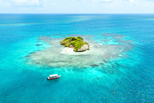 Aerial view of a small tropical islet surrounded by turquoise coral reefs and a boat in the Caribbean Sea, English Harbour, Saint Paul, Antigua and Barbuda.