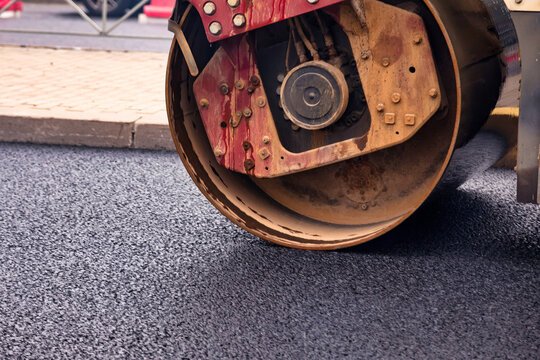 Workers are busy paving an urban road with asphalt. A heavy roller compactor is leveling the surface for a durable finish. This is part of a larger street improvement project.