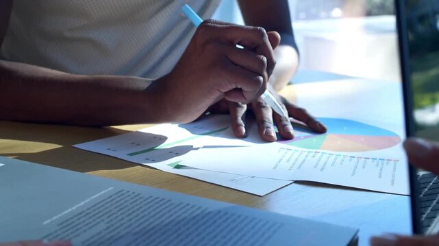 Close-up view of business partners analyzing a colorful printed pie chart document on a desk during a corporate strategy meeting.