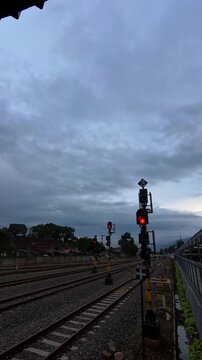 Vertical video of Train station platform under a metal roof. Red signal lights indicate train movement stopped. Yellow safety rails line the platform edge. Blue sign directs passengers to exit. 4K Foo