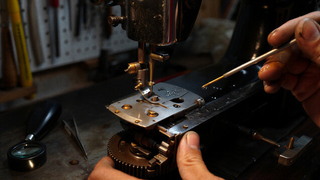 Close up of a person using a thin metal tool to oil the internal mechanical parts of a vintage black sewing machine in a workshop setting