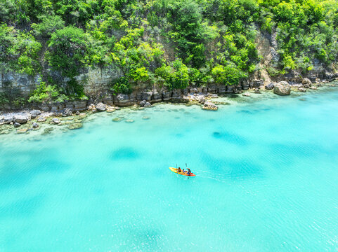 Aerial view of people in a yellow kayak paddling through turquoise water along the lush green cliffs of English Harbour, Saint Paul, Antigua and Barbuda.