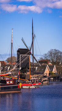 Traditional Dutch windmill overlooking boats in a historic harbor in the Netherlands. Scenic waterfront, maritime heritage and authentic Dutch architecture under a blue sky.