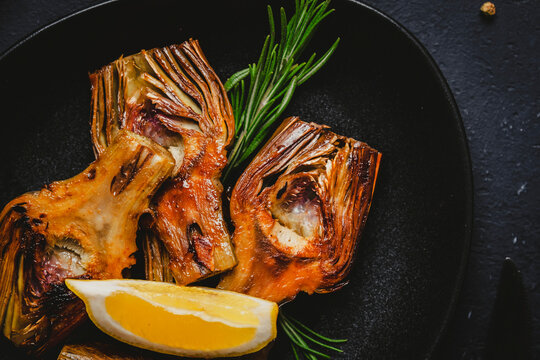 Cooked Italian carciofi with savory seasoning and organic herbs on black dinnerware. Gourmet restaurant catering and wholesome plant based dieting concept, horizontal macro view.