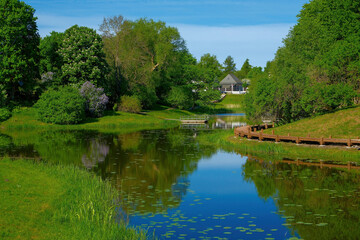 Obraz premium Cozy cottage house on a hill overlooking a calm river in a lush green spring park. Scenic countryside architecture.