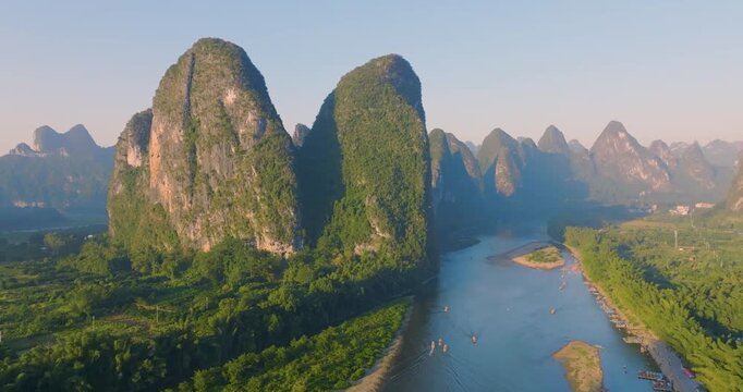 Forward aerial drone view of Guilin Li River karst mountains at sunrise, golden sun rays across limestone peaks, drifting fishing boat on winding river, iconic Guilin natural landscape, Guangxi China