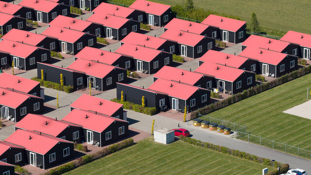 Aerial view of rows of modern black houses with vibrant red roofs and small gardens in a residential complex Luttelgeest, Flevoland, Netherlands.