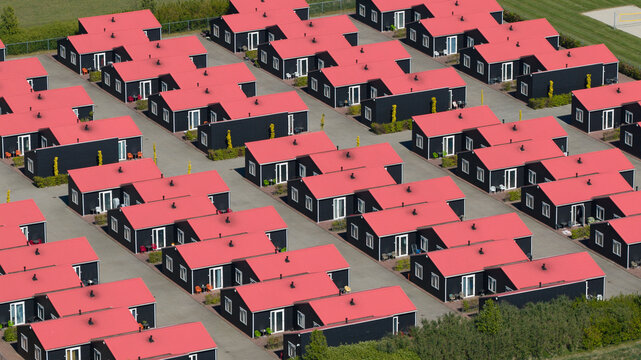 Aerial view of rows of identical modern houses with black walls and bright red roofs in a residential complex in Luttelgeest, Flevoland, Netherlands.