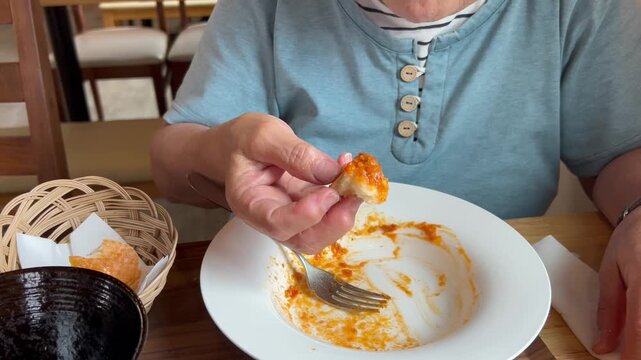 パスタソースをつけてパンを食べる高齢女性