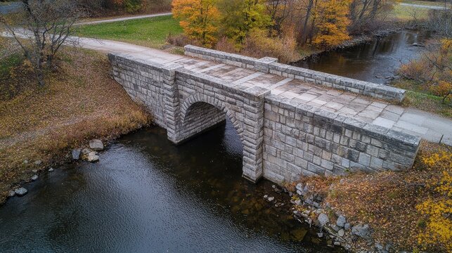 Historic stone bridge arch geometry showcasing classic American masonry construction over peaceful river with vibrant autumn foliage natural background