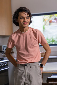 Indian teenage male wearing textured pink shirt and pearl necklace, standing in modern kitchen