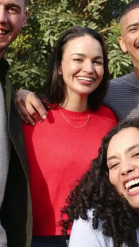 Vertical video: Smiling 4 friends posing by hedge on cam cue for portrait with red-sweater necklace