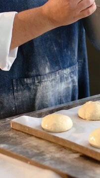 Vertical video: Tilting mix bowl, baker in chef sleeve brushing buns at counter with brush to glaze