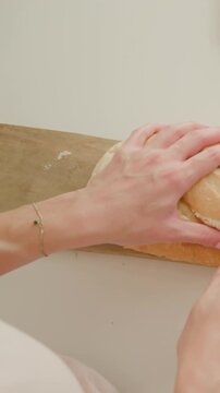 Vertical video: Positioning knife, hands holding loaf and sawing on cutting board to slice in top