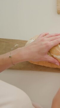 Vertical video: Slicing hands making first cut and sawing loaf with knife on counter, serving