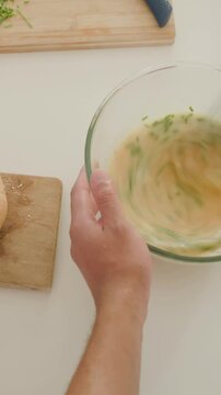 Vertical video: Steadying bowl, cook whisking egg-herb mix with whisk in kitchen for batter