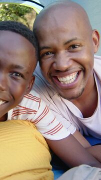Vertical video: Cam starting, smiling dad and teen leaning in tent on mustard pillow, wearing tees