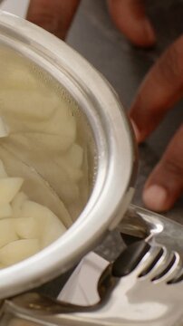 Vertical video: Entering right hand steadying steel pot at stove, preparing to lift with steamer