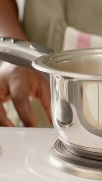 Vertical video: Reaching cook's hand steadying steel pan on stove for cooking, showing pink apron