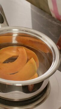 Vertical video: Reaching hand monitoring and adjusting pot on stovetop with orange slices, pink top