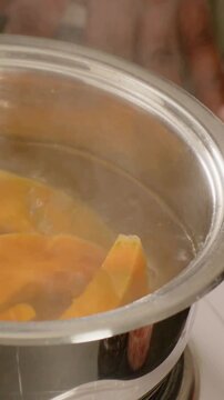 Vertical video: Hotplate heating pot with glass rim simmering pumpkin wedges on counter, plate
