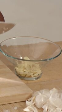 Vertical video: Holding clove, hands peeling and slicing garlic at counter for meal with blue knife