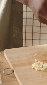 Vertical video: Lowering cook hands holding blue knife, chopping garlic on board into glass bowl