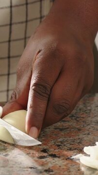 Vertical video: Knife starting cut, hand wearing checked apron slicing onion on counter for meal