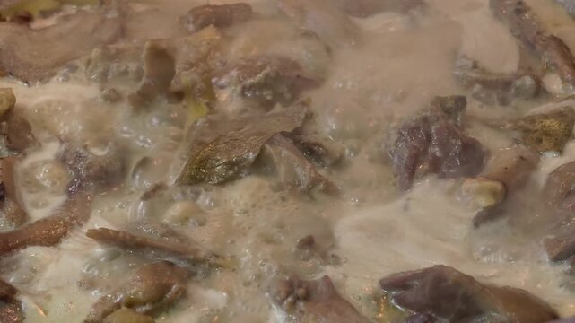 Close up of a bubbling chicken stew simmering in a creamy white sauce with a visible bay leaf, showing the slow cooking process of a traditional homemade meal in a professional kitchen style