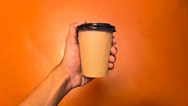 Male or men hand holding paper cup of take away drinking coffee. orange floor on the background. front, side. top view, high angle, above, flat lay. bright. isolated. eco, lifestyle.