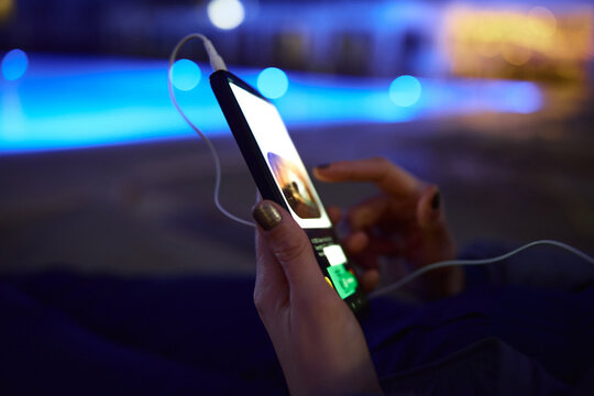 Woman using smartphone by pool at night &ndash; glowing screen, copy space, modern lifestyle