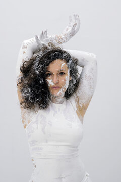 Portrait of a woman covered with white paint standing against a bright background with expressive pose intense gaze and artistic body textures creating a contemporary concept scene