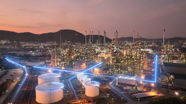 Glowing blue digital network lines flowing through a massive oil refinery and petrochemical plant at twilight. Smart factory technology, IoT infrastructure, and modern energy data management.