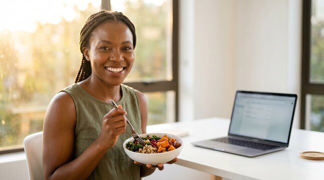 Smiling African American woman eating healthy meal at desk with laptop.