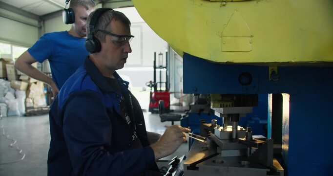 Punch press operator working at metal stamping machine while engineer supervisor observes process in industrial workshop