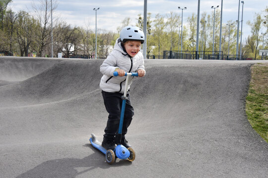Young boy riding a blue scooter at a skatepark wearing a helmet and